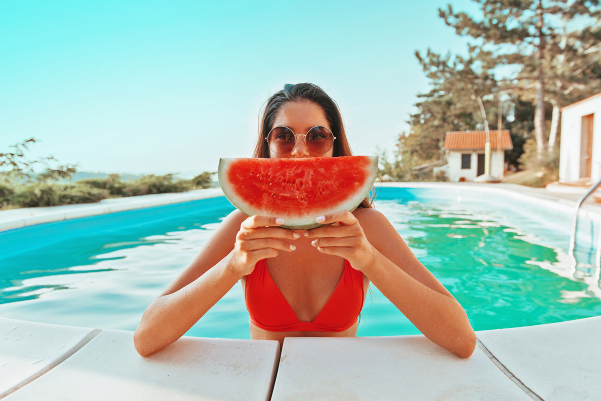 Woman eating watermelon in pool after spray tanning session